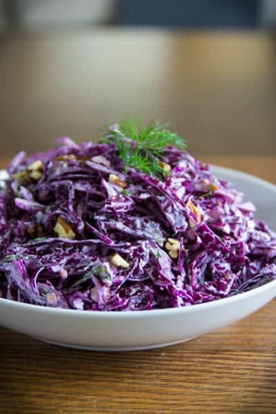 purple cabbage salad in a white plate with walnuts and dill on top