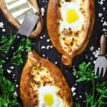 2 easy khachapuri breads with eggs in the center and sliced feta cheese and parsley beside it