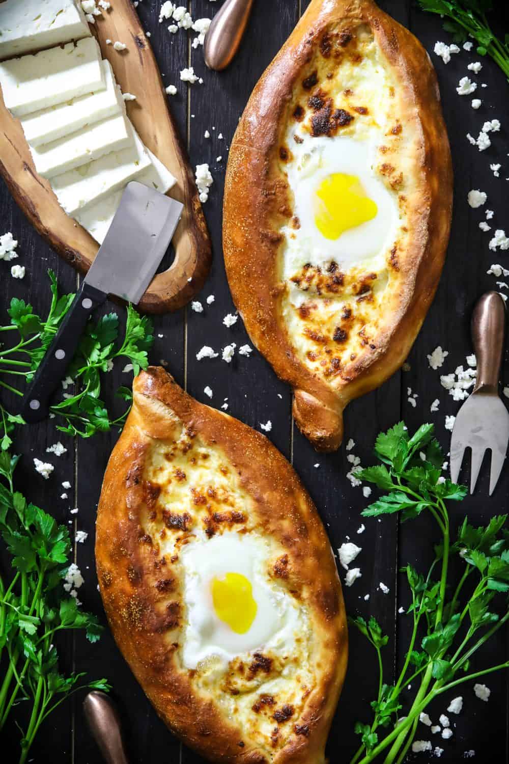 2 easy khachapuri breads with eggs in the center and sliced feta cheese and parsley beside it