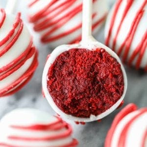 red velvet cake pops dipped in white candy melts and drizzled with red candy melts, then bitten into