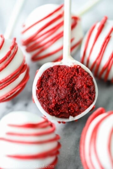 red velvet cake pops dipped in white candy melts and drizzled with red candy melts, then bitten into