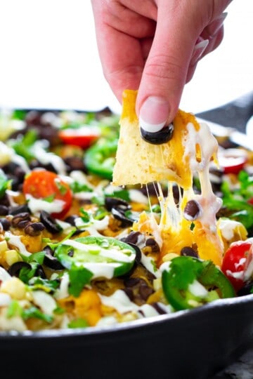 a close up shot of chicken nachos with a tortilla chip and cheddar cheese being pulled out of the skillet