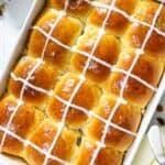 overhead image of fluffy brioche hot cross buns in a white baking dish with butter beside it