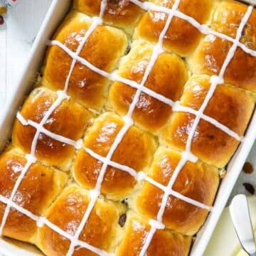 overhead image of fluffy brioche hot cross buns in a white baking dish with butter beside it