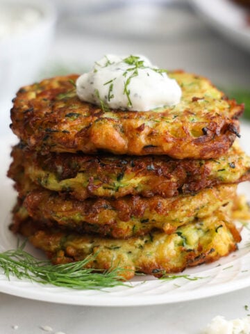 Stack of Zucchini Fritters with a dollop of tzatziki sauce on top and some fresh dill