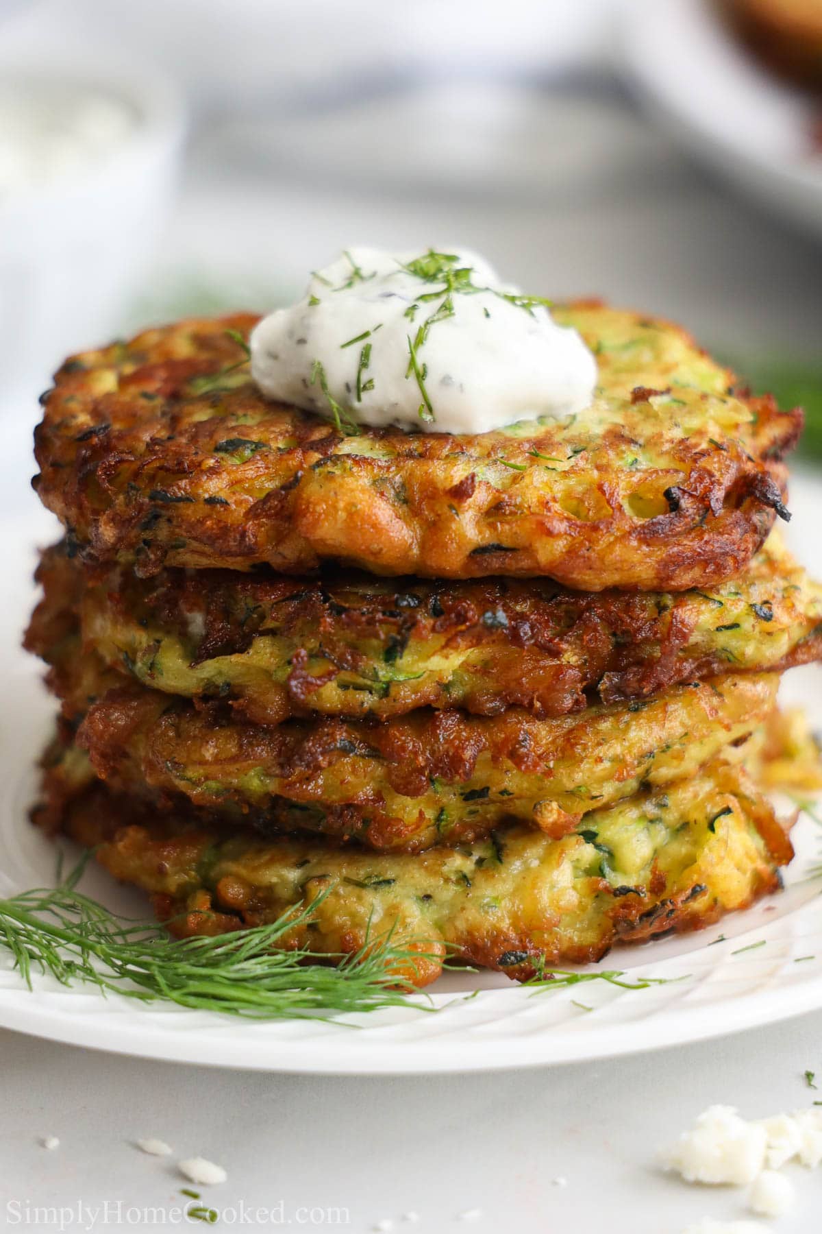 Stack of Zucchini Fritters with a dollop of tzatziki sauce on top and some fresh dill 