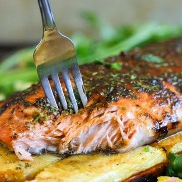 grilled salmon on a cedar plank with pineapples under and a fork piercing through the fish