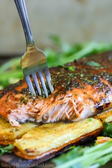 grilled salmon on a cedar plank with pineapples under and a fork piercing through the fish