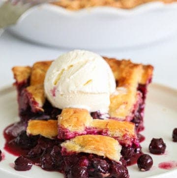 close up image of sliced homemade blueberry pie with a lattice top and vanilla ice cream on top