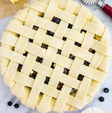 overhead image of homemade blueberry pie with a lattice pie crust on a white background