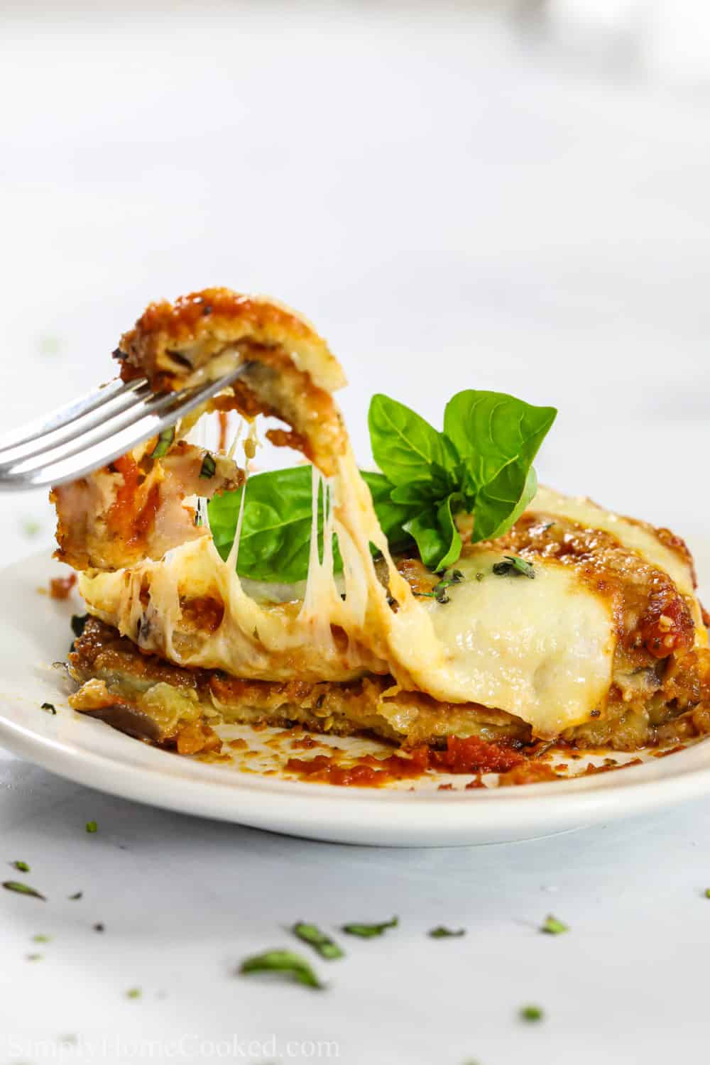 a piece of baked eggplant parmesan on a plate and a fork removing a bit with a cheese pull