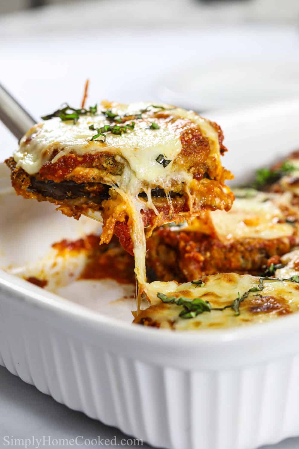 a spatula lifting a piece of eggplant parmesan over a casserole dish