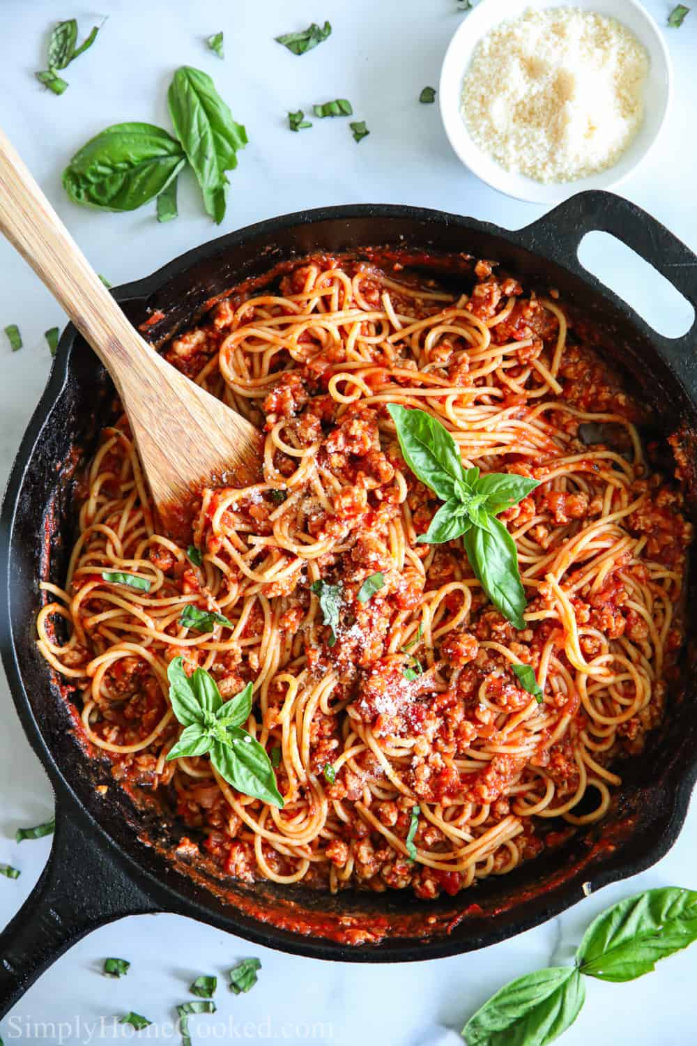 overhead image of spaghetti and meat sauce in a cast iron pan with fresh basil on top