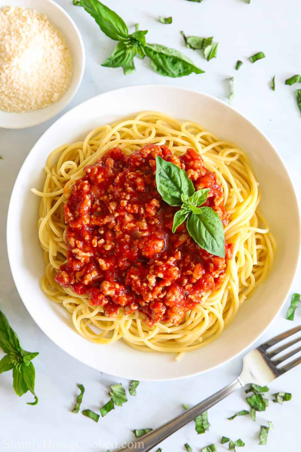 overhead image of spaghetti on a white plate with homemade meat sauce and fresh basil on top with a fork beside it