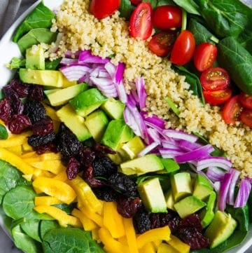 overhead shot of spinach salad in a white plate with quinoa, tomatoes, avocado, and red onion on top