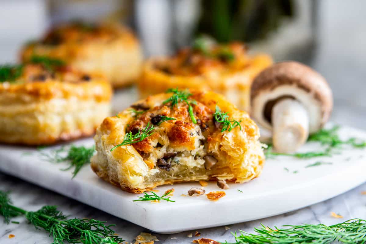 Image of four mushroom puff pastry appetizers with a mushroom and some fresh dill on a white plate.