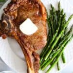 overhead image of ribeye steak on a white plate with asparagus and brussels sprouts beside it.