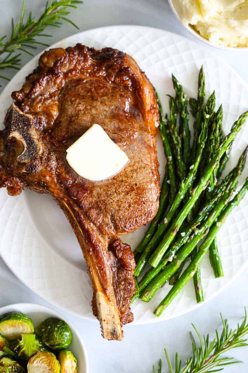 overhead image of ribeye steak on a white plate with asparagus and brussels sprouts beside it.