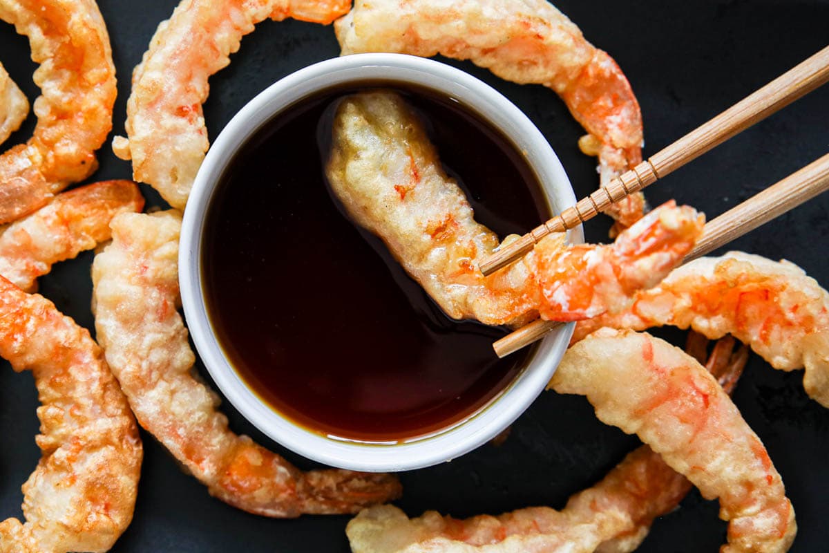 Chopsticks dipping shrimp tempura into Tempura Dipping Sauce with more shrimp tempura nearby.