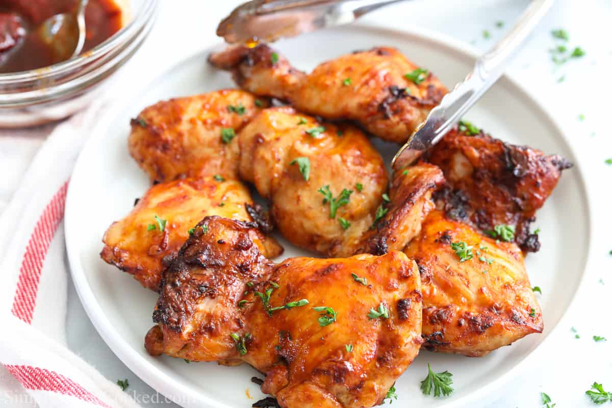 Close up of plate with Air fryer Chipotle Chicken Thighs and tongs on the side, sauce in the background.