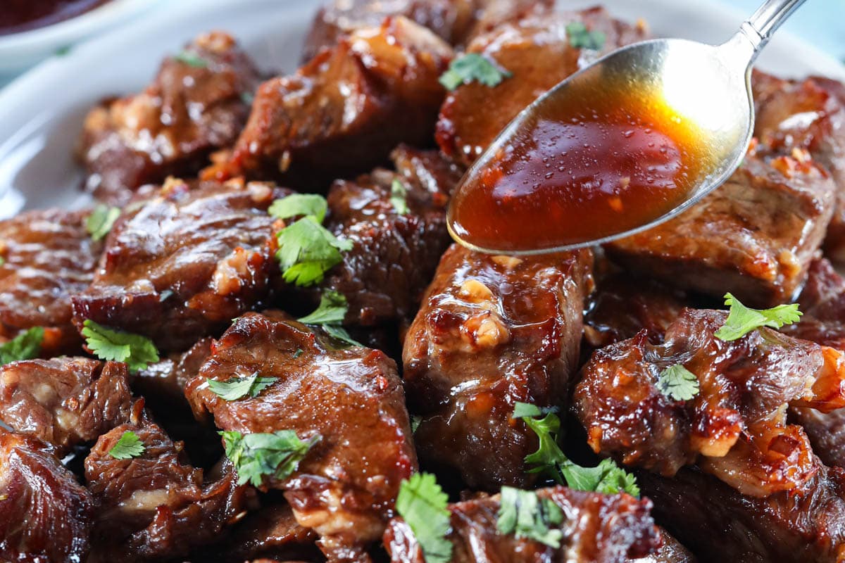 These Juicy Air Fryer Steak Bites are mouth-wateringly scrumptious. Full of flavor, you'll love the savory taste and great texture of these tender steak bites. #steakbites #airfryersteak #airfryersteakbites #airfryersteakbitesrecipe A spoon drizzling sauce on Air Fryer Steak Bites.