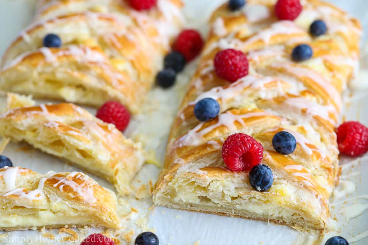 Two cheese danishes sliced and covered with berries on a white background.