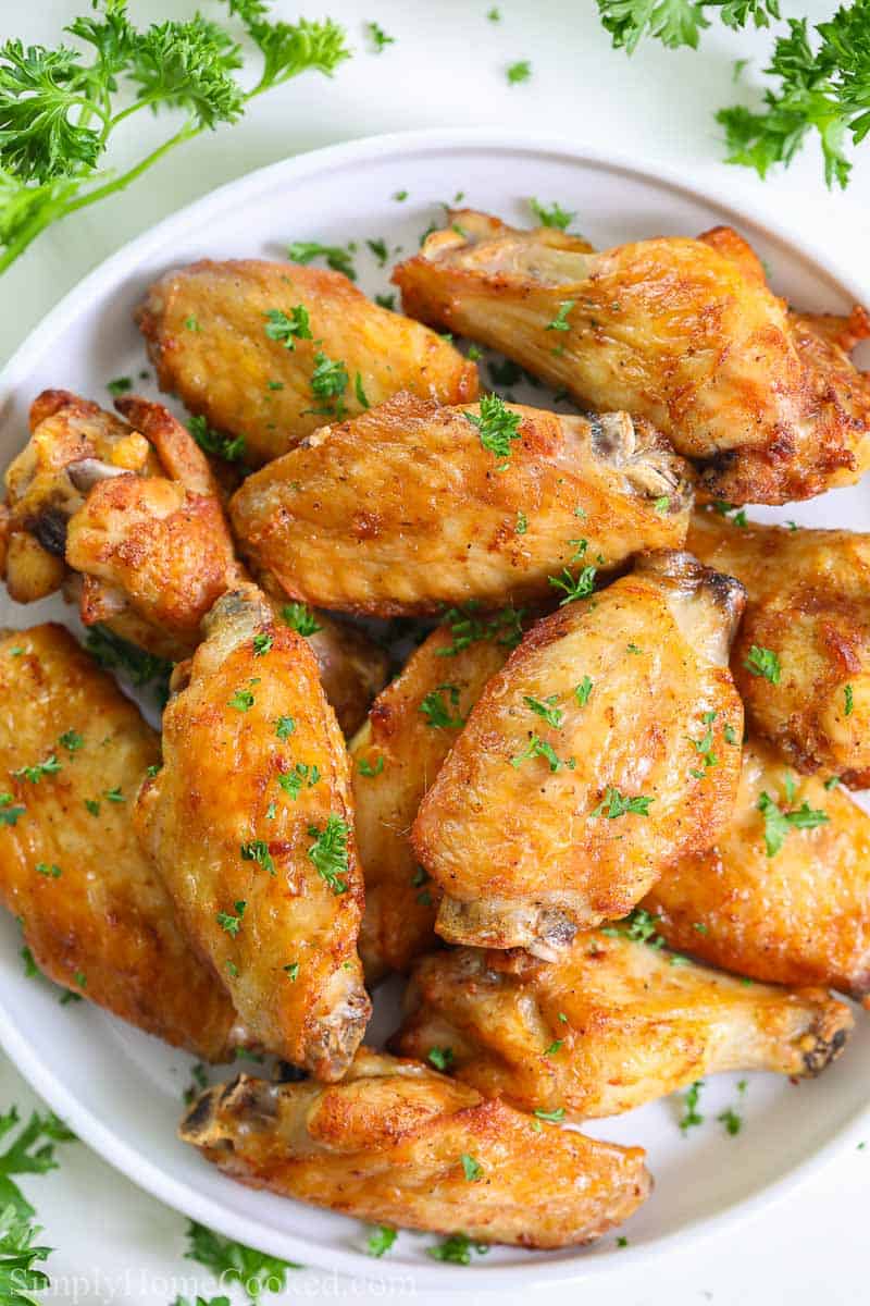 overhead image of crispy air fryer chicken wings on a white plate with chopped parsley on top