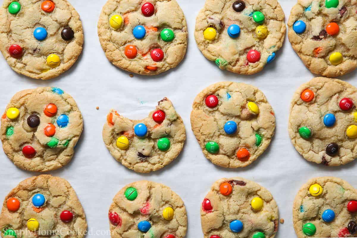 Chewy M&M cookies on a baking sheet, one with a bite taken out.