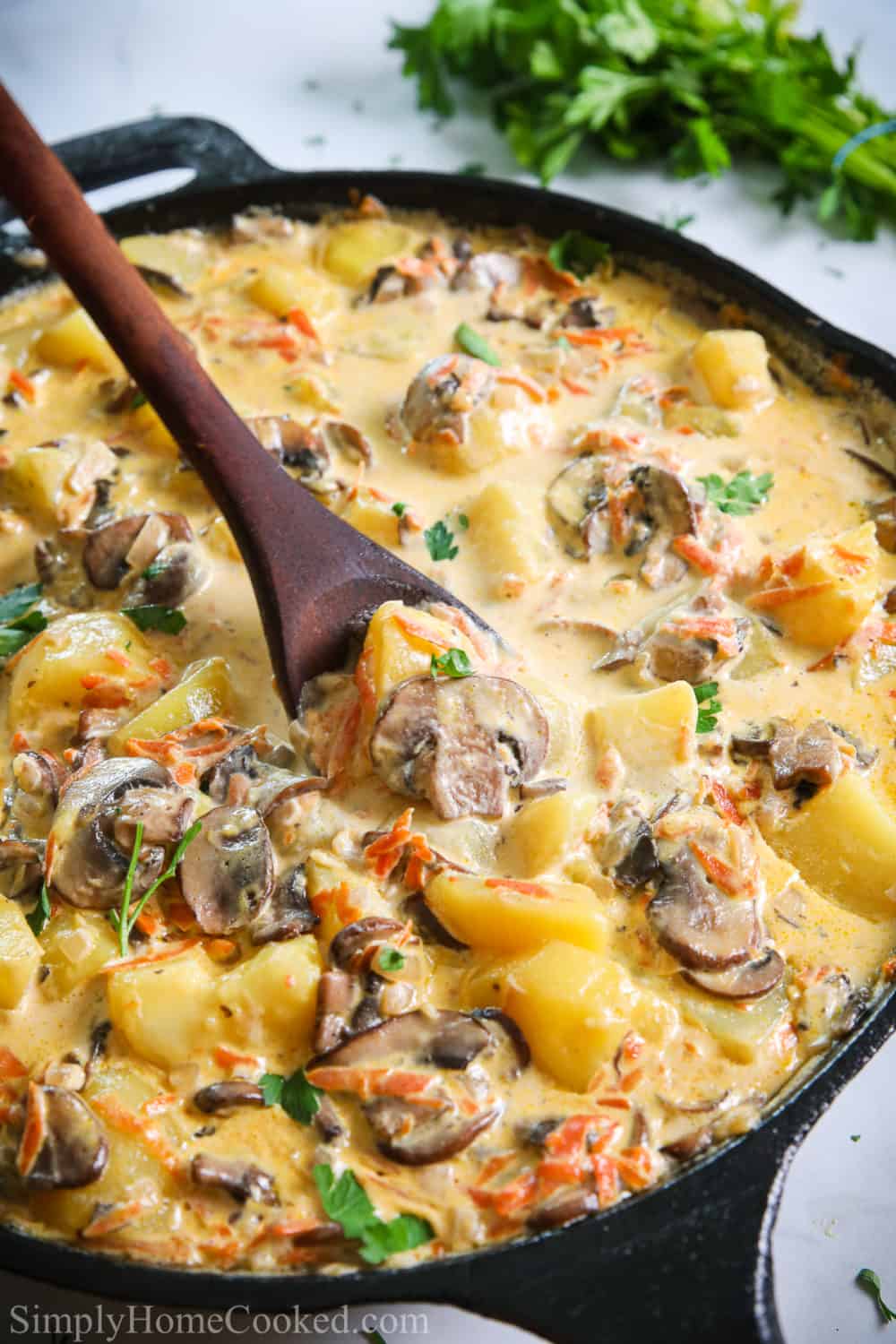 Potatoes with Mushroom Gravy in a black skillet with a wooden spoon mixing it and parsley inn the background.