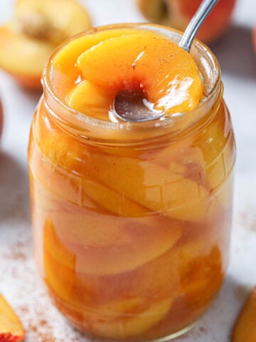 Spoon lifting out a slice of peach from Peach Pie Filling in a jar.