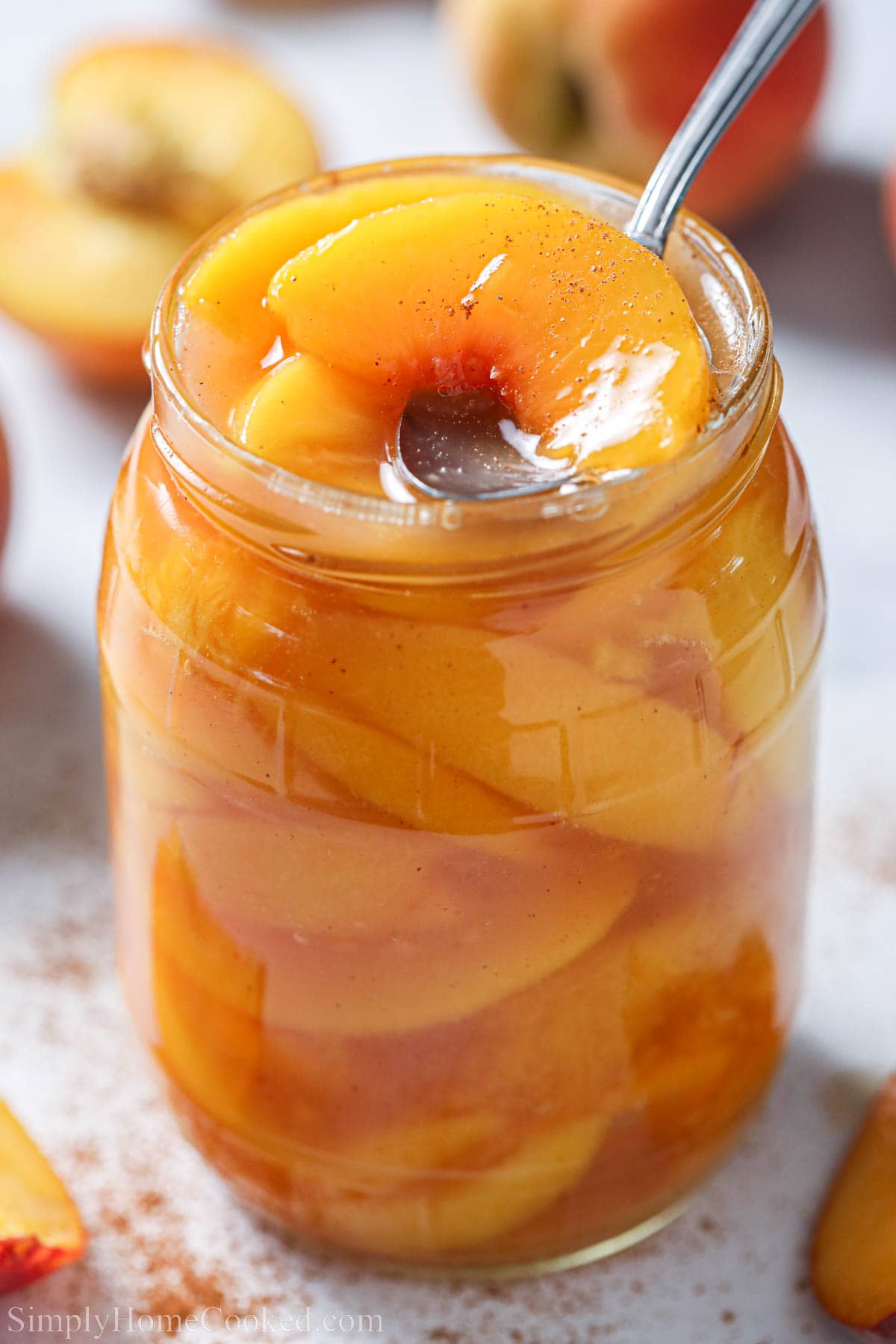 Spoon lifting out a slice of peach from Peach Pie Filling in a jar. 