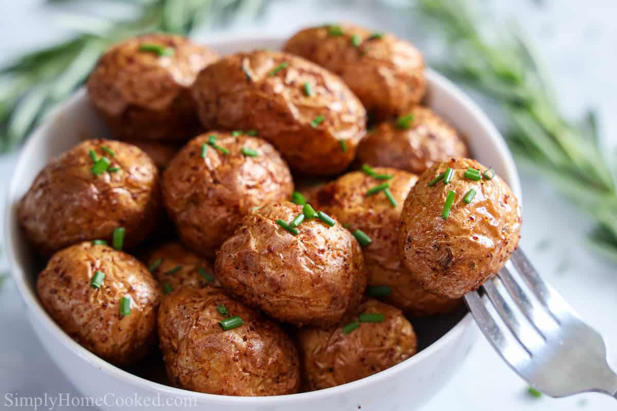 Bowl of Crispy Air Fryer Baby Potatoes with garnish and a fork on the side.