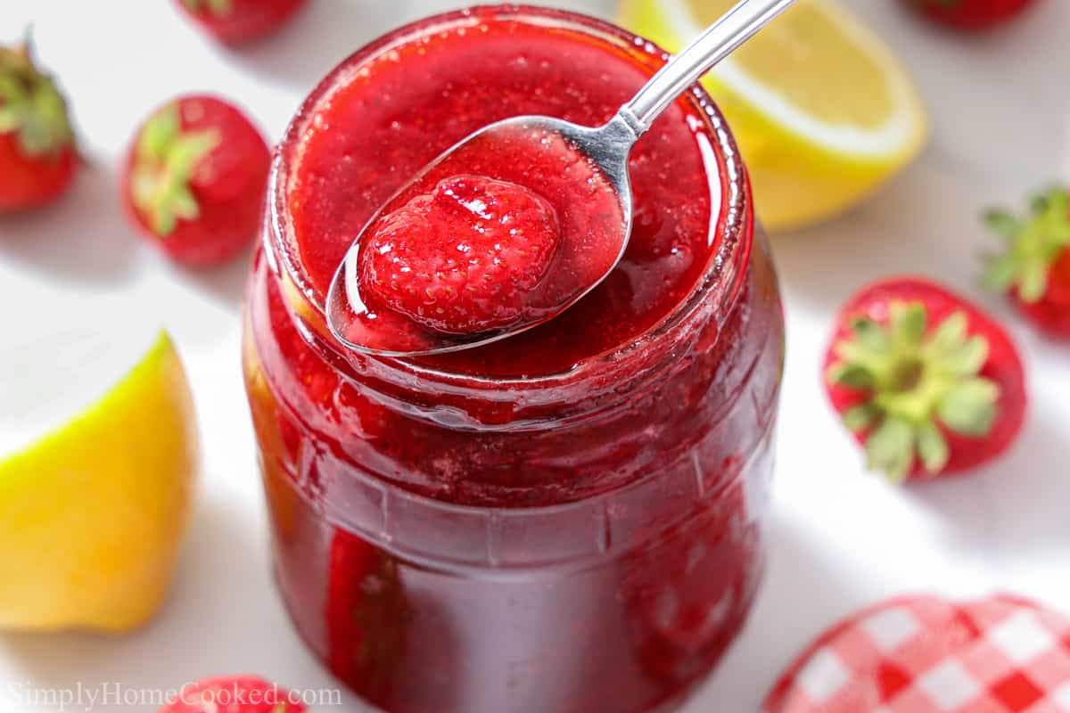 a overhead image of homemade strawberry jam in a glass mason jar with a spoon full of strawberry jam in it