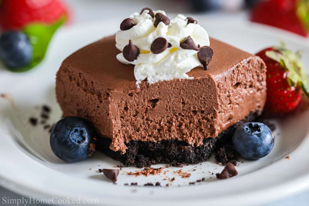 A close up image of a No-bake Chocolate Cheesecake Bar with blueberries and strawberries around it.