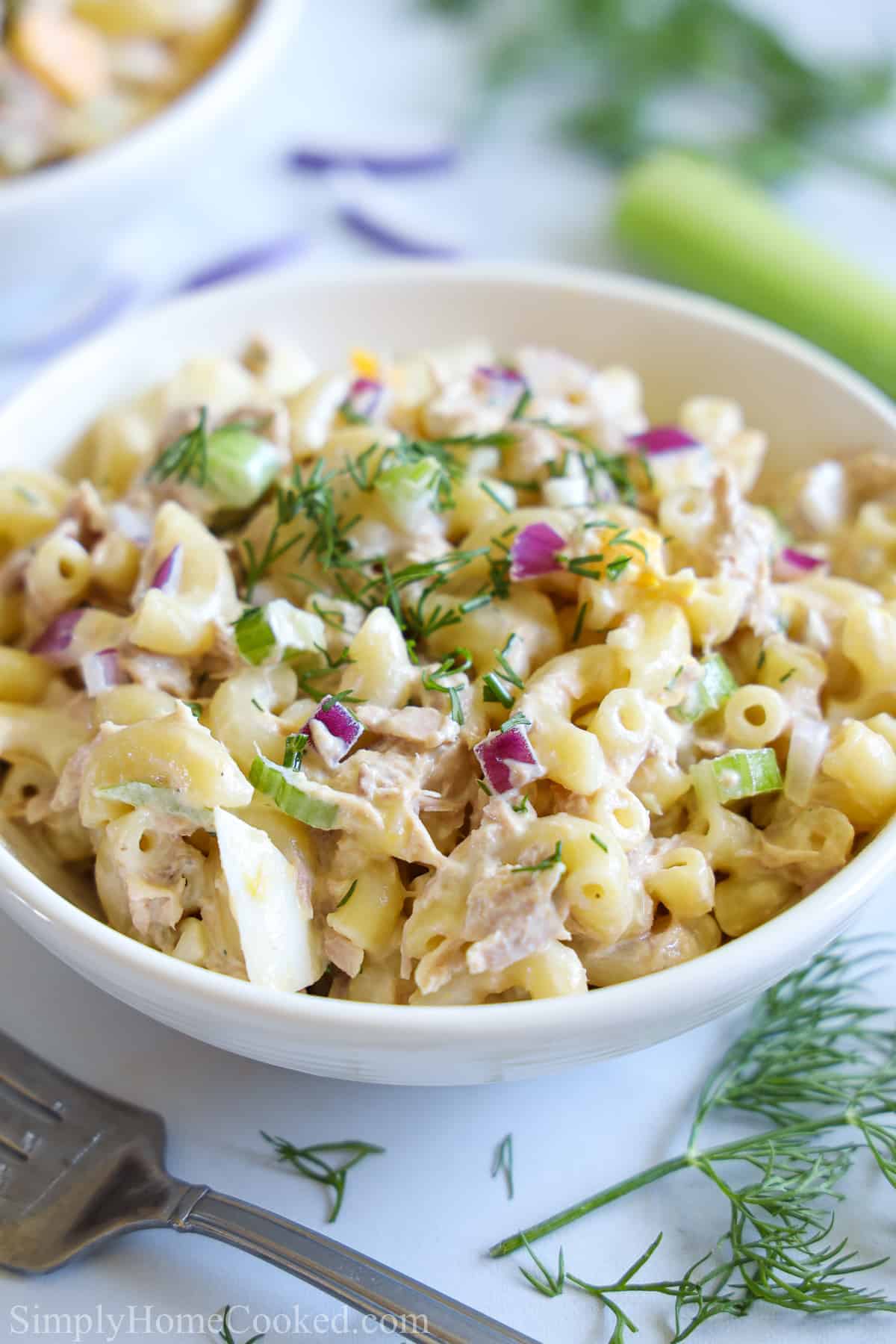 White bowl of Tuna Pasta Salad with celery, a fork, and dill in the background.