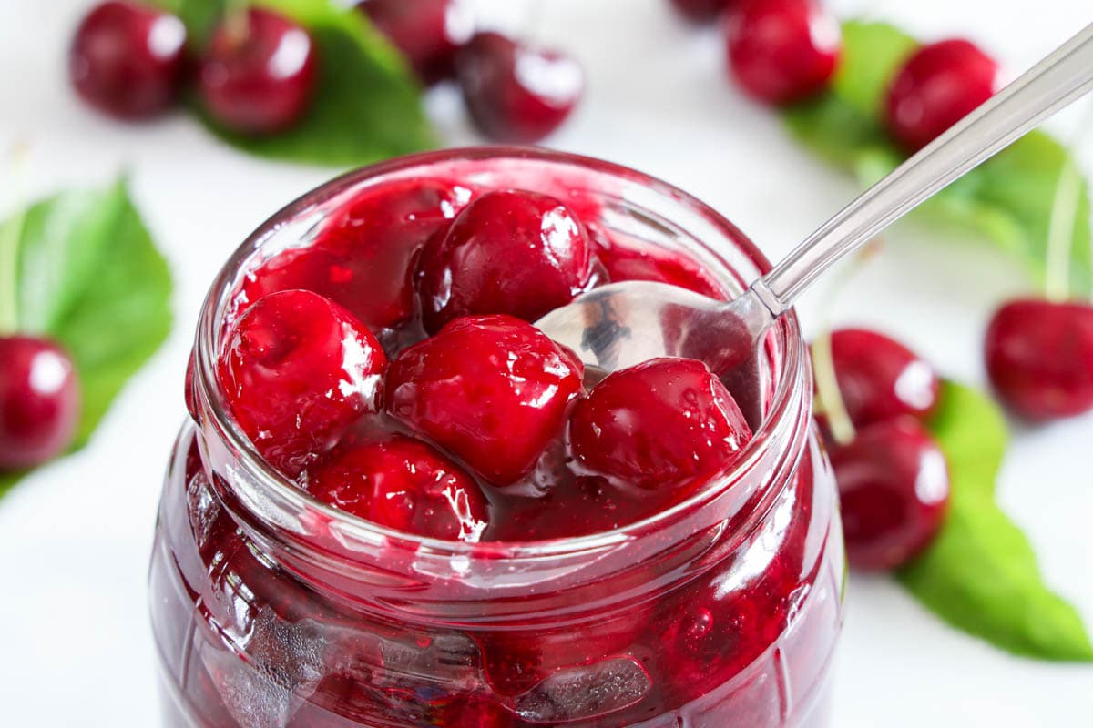 A spoon lifting out some Cherry Pie Filling from a jar. 