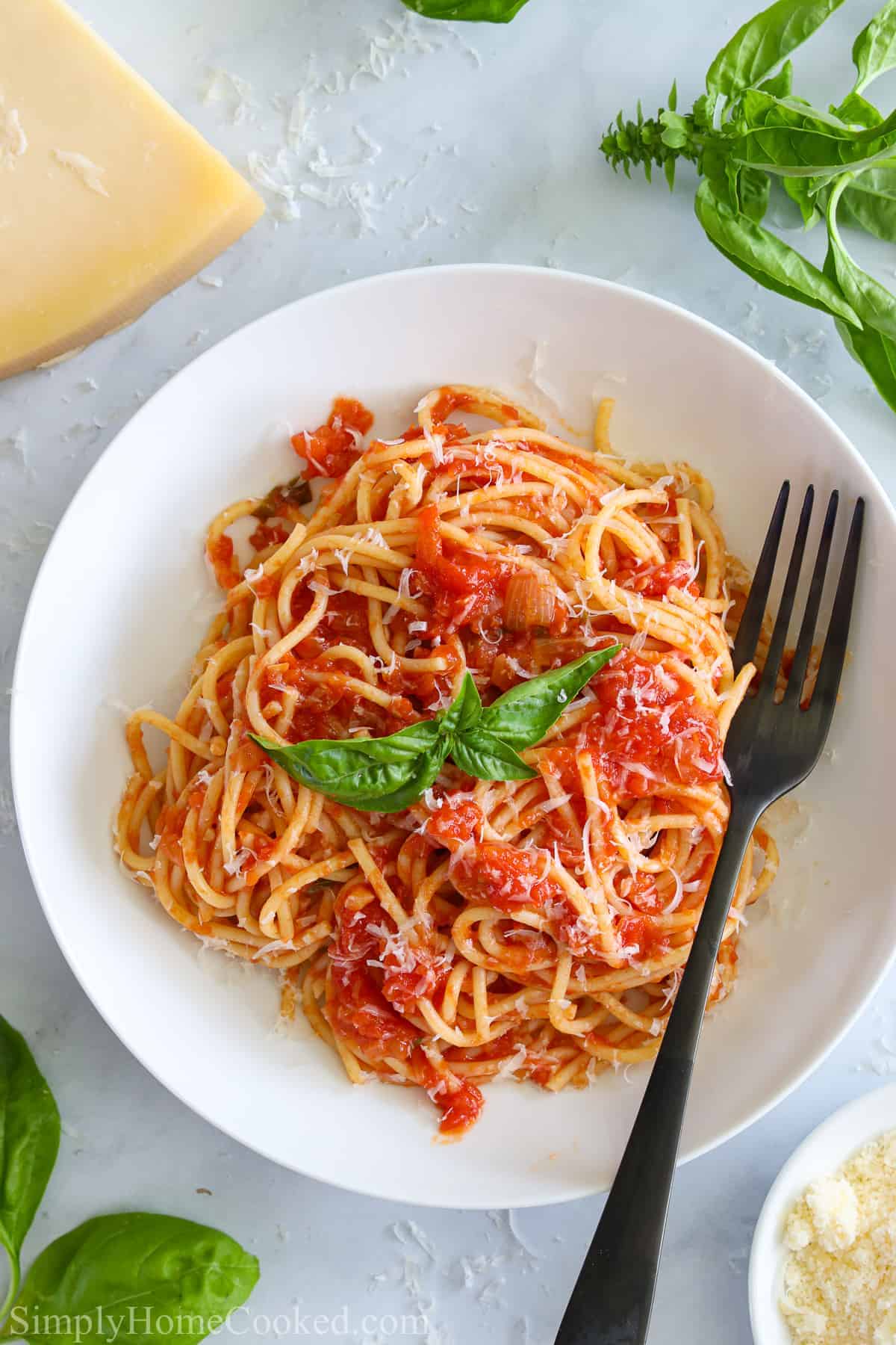 Pasta Pomodoro on a white plate with a fork and Parmesan cheese and basil nearby.