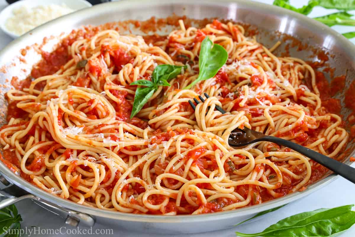 Pan of Pasta Pomodoro with a fork twirling the pasta and basil leaves on top and to the side.