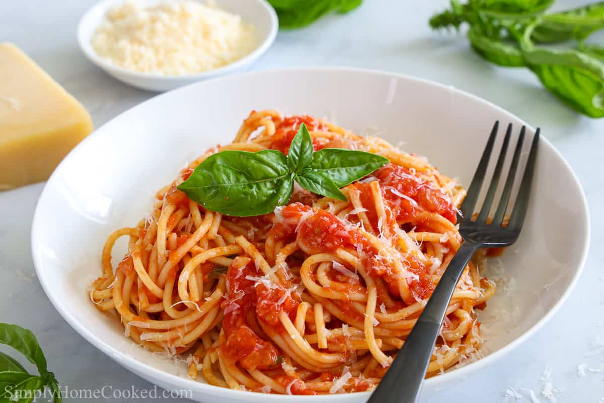 Plate of Pasta Pomodoro with a fork and basil leaves, and Parmesan cheese and basil in the background.