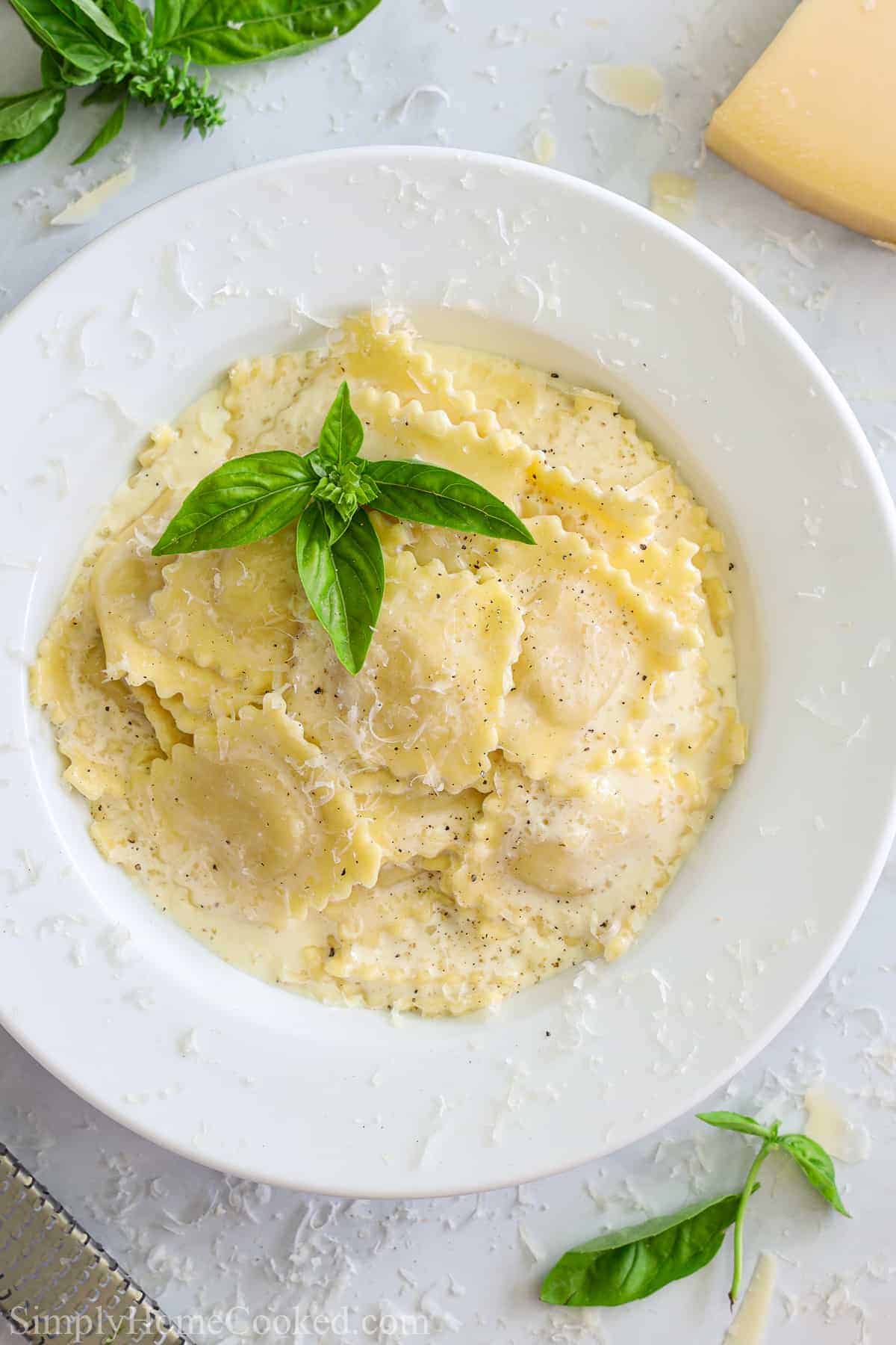 White plate of Easy Four Cheese Ravioli with herbs on top and some herbs and Parmesan cheese to the side.