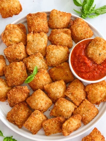 Plate of Crispy Fried Ravioli, with one in a marinara dipping sauce.