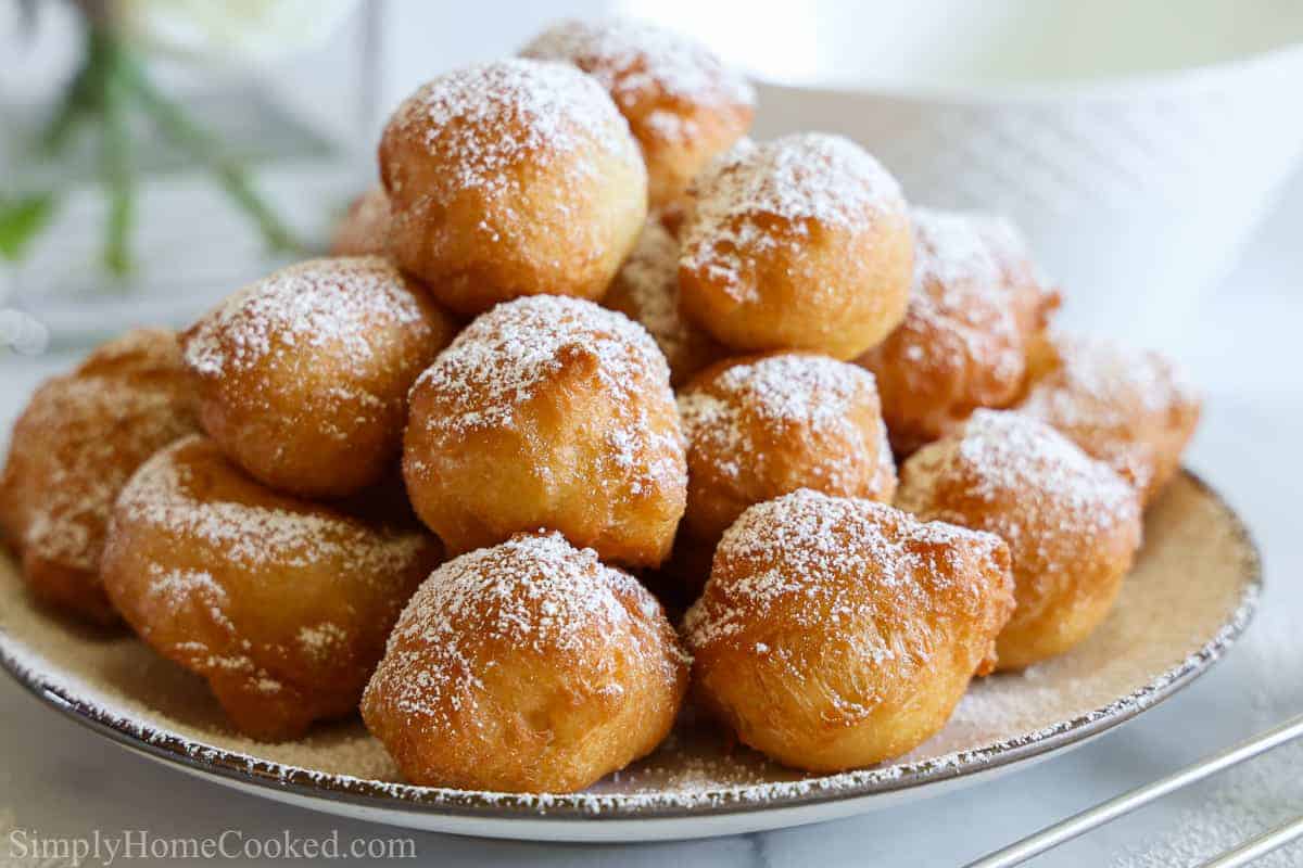 Plate full of Italian donuts - Zeppoles - that are dusted with powdered sugar.