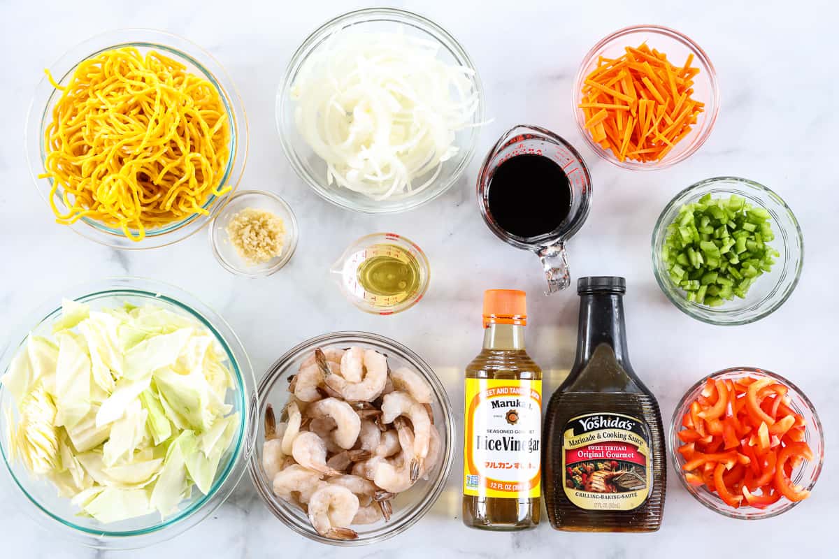 Ingredients for 30-Minute Shrimp Chow Mein, including yakisoba noodles, onion, carrot, celery, garlic, red pepper, shrimp, cabbage, soy sauce, teriyaki marinade, and rice vinegar, on a white background.