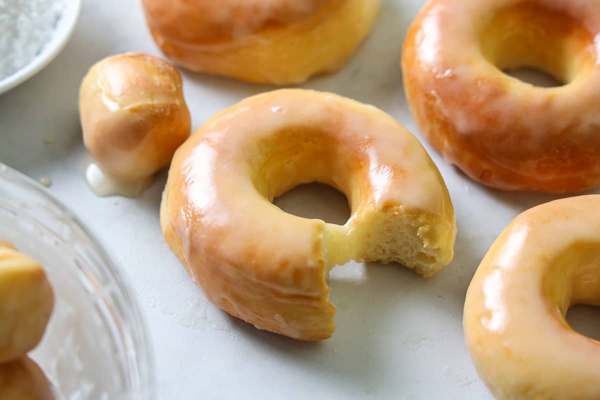 Glazed Air Fryer Donuts on a white background with donut holes and one donut missing a bite.