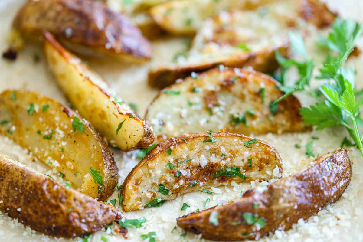 These Garlic Parmesan Air Fryer Potato Wedges have the perfect combo of salty cheese & flavorful garlic. They're crispy & delicious, perfect to eat on their own or as a side dish. #healthyairfryerpotatowedges #potatowedgesrecipe #airfryerpotatowedgesrecipe #garlicparmesanairfryerpotatowedgesrecipe Close up of Garlic Parmesan Air Fryer Potato Wedges garnishes with parsley.