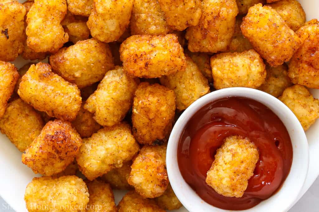 Close up of a plate of Crunchy Air Fryer Tater Tots with one in a dish of ketchup.