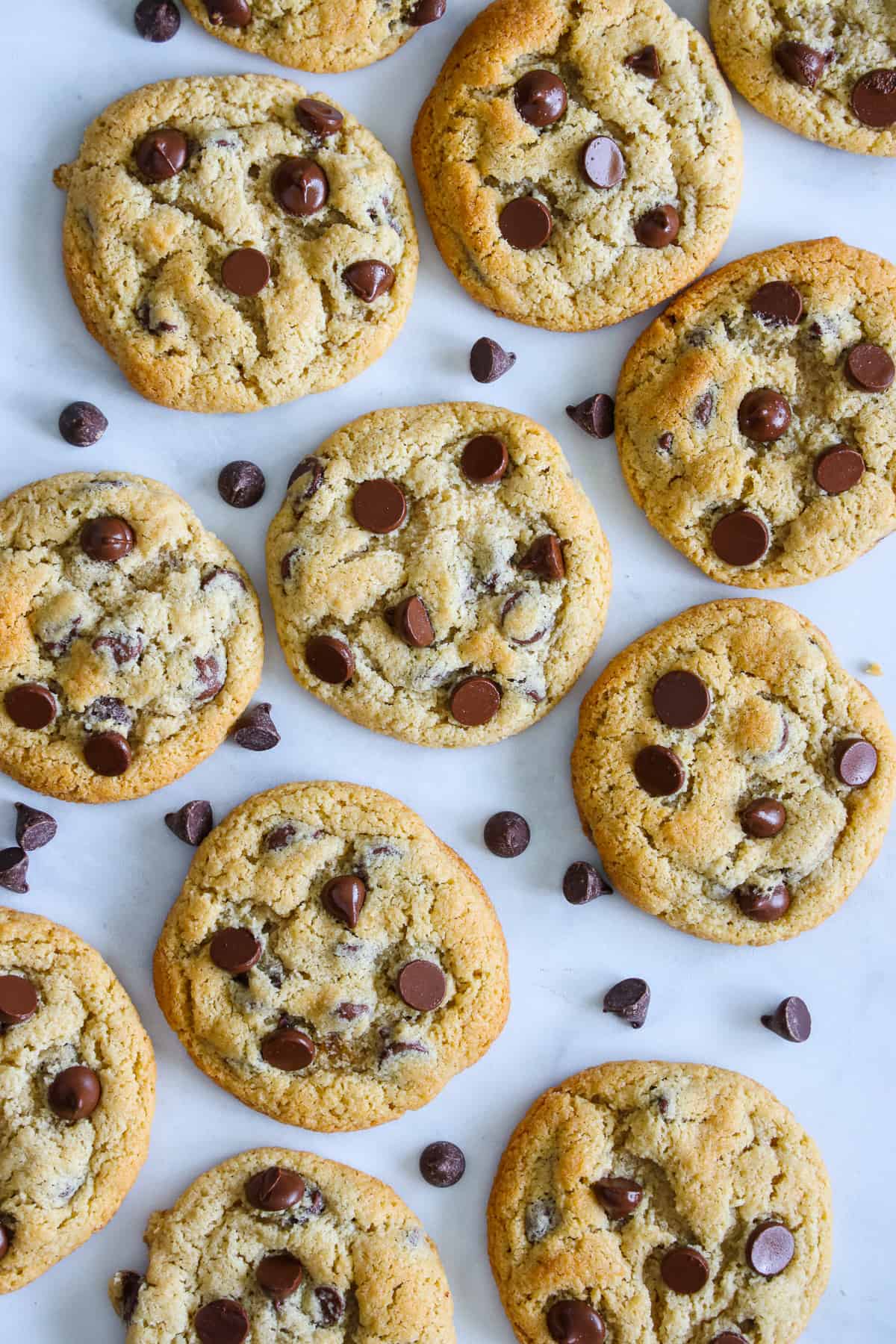 These gooey, chocolaty gluten-free cookies are perfect for freezing or serving hot out of the oven. Almond Flour Chocolate Chip Cookies are gluten free, so easy, and can be made in advance. #freezercookies #freezerglutenfreecookies #freezerchocolatechipcookies #freezeralmondflourchocolatechipcookies Overhead view of Almond Flour Chocolate Chip Cookies with a scattering of chocolate chips nearby.