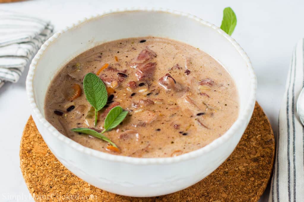 Creamy Chicken and Wild Rice Soup in a white bowl with garnish, sitting on a corkboard placemat.