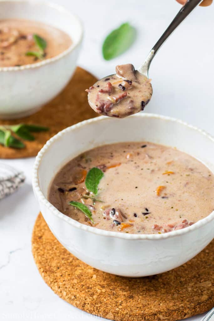 Bowl of Creamy Chicken and Wild Rice Soup with a soupful held above and another bowl in the background.