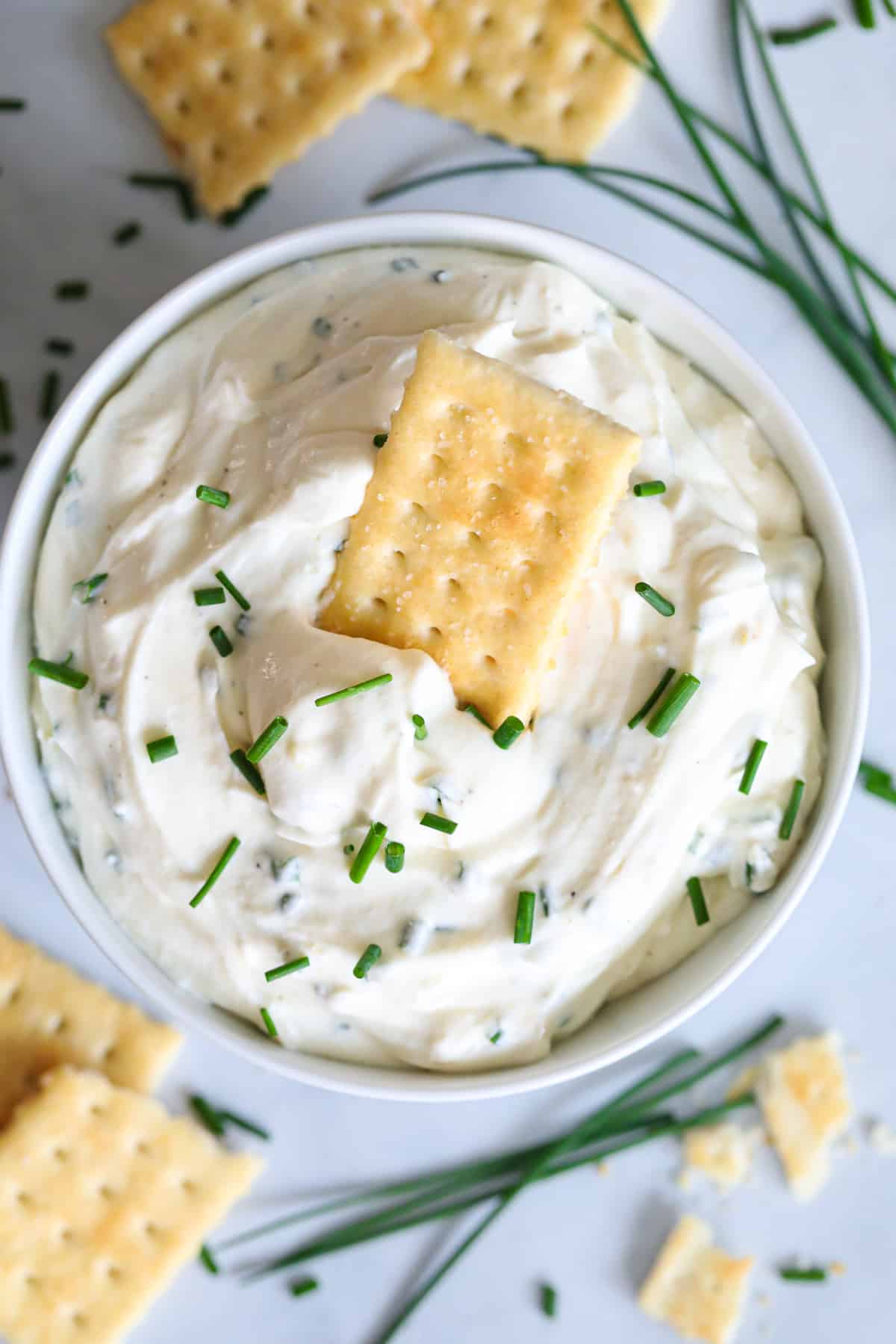 Aerial view of Garlic Cream Cheese Dip with a cracker in it and more on the side, with chopped chives on top.